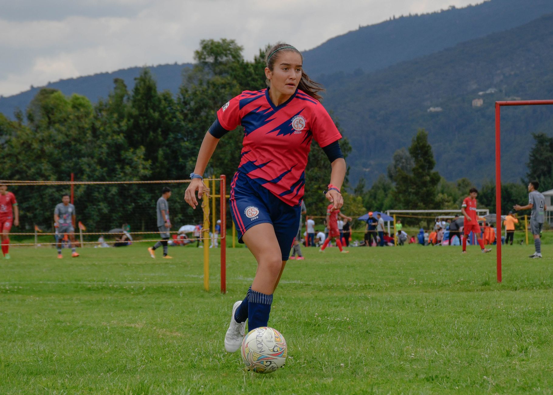 Focused young female soccer player dribbling on a lush green field during a daytime match.