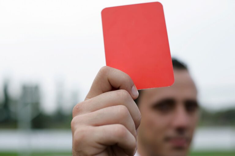 Close-up of a referee holding a red card, signaling a penalty in a soccer match.