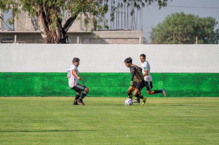 Competitive soccer game featuring young men in action on a sunny outdoor pitch.