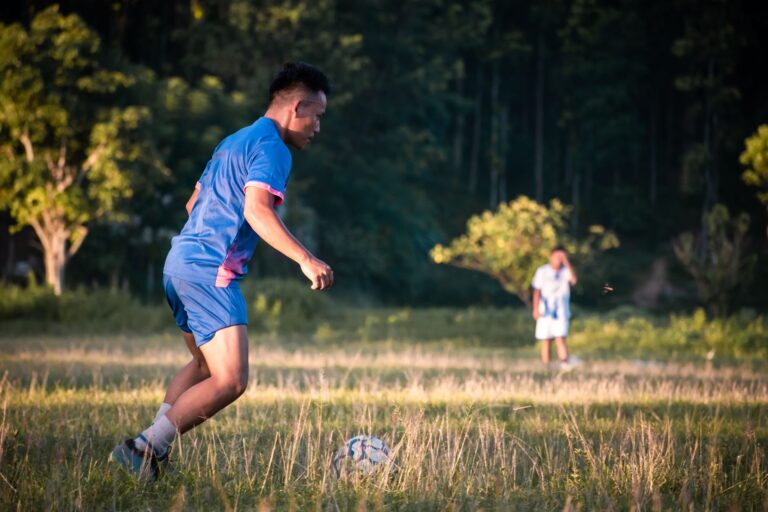 A young adult playing soccer on a grassy field with trees in the background.