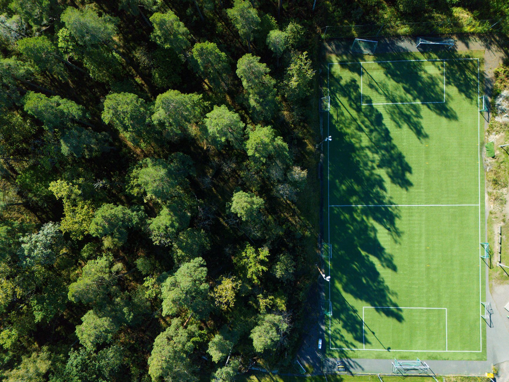 Aerial view of a lush forest beside a soccer field in Jönköping, Sweden.