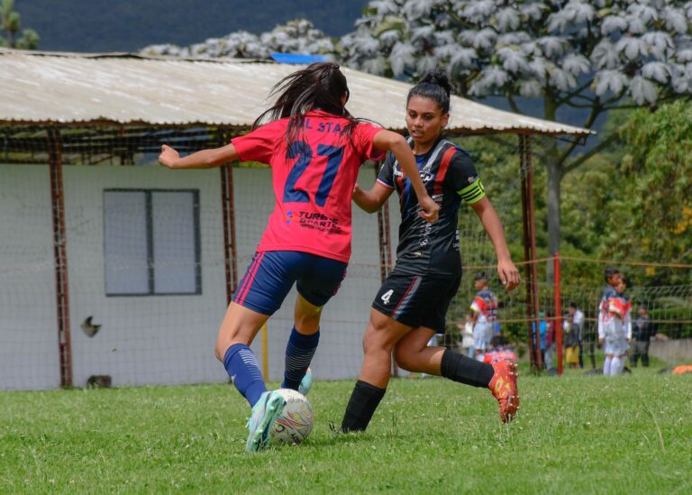 Competitive women's soccer match with players in action outdoors on green field.