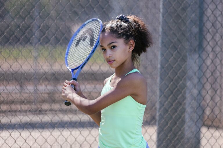 Focused young girl practicing tennis on an outdoor court with racquet.