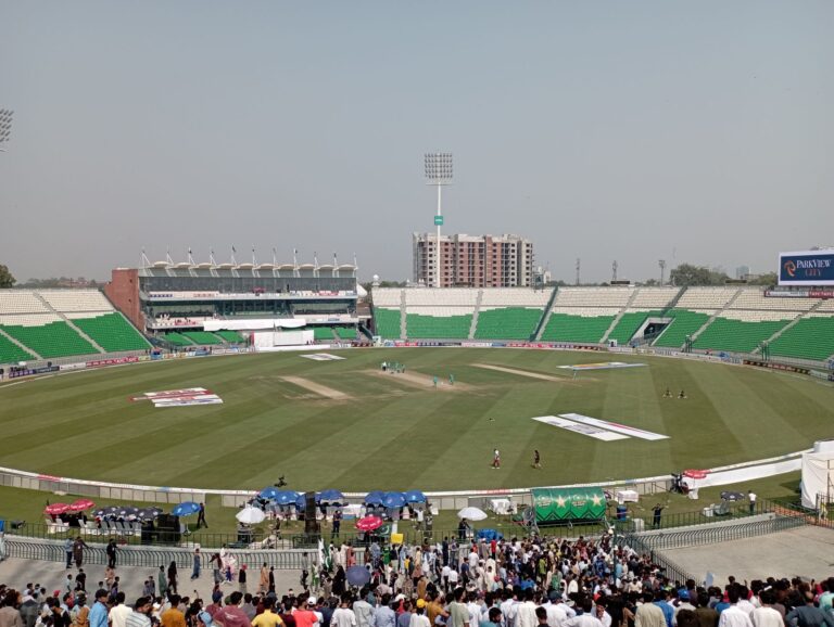 Vibrant cricket match at a large stadium filled with enthusiastic spectators under a bright sky.