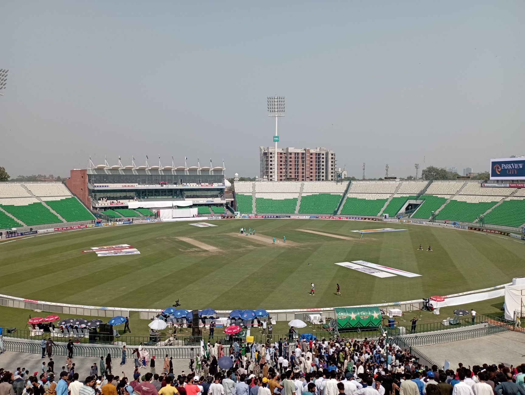 Vibrant cricket match at a large stadium filled with enthusiastic spectators under a bright sky.
