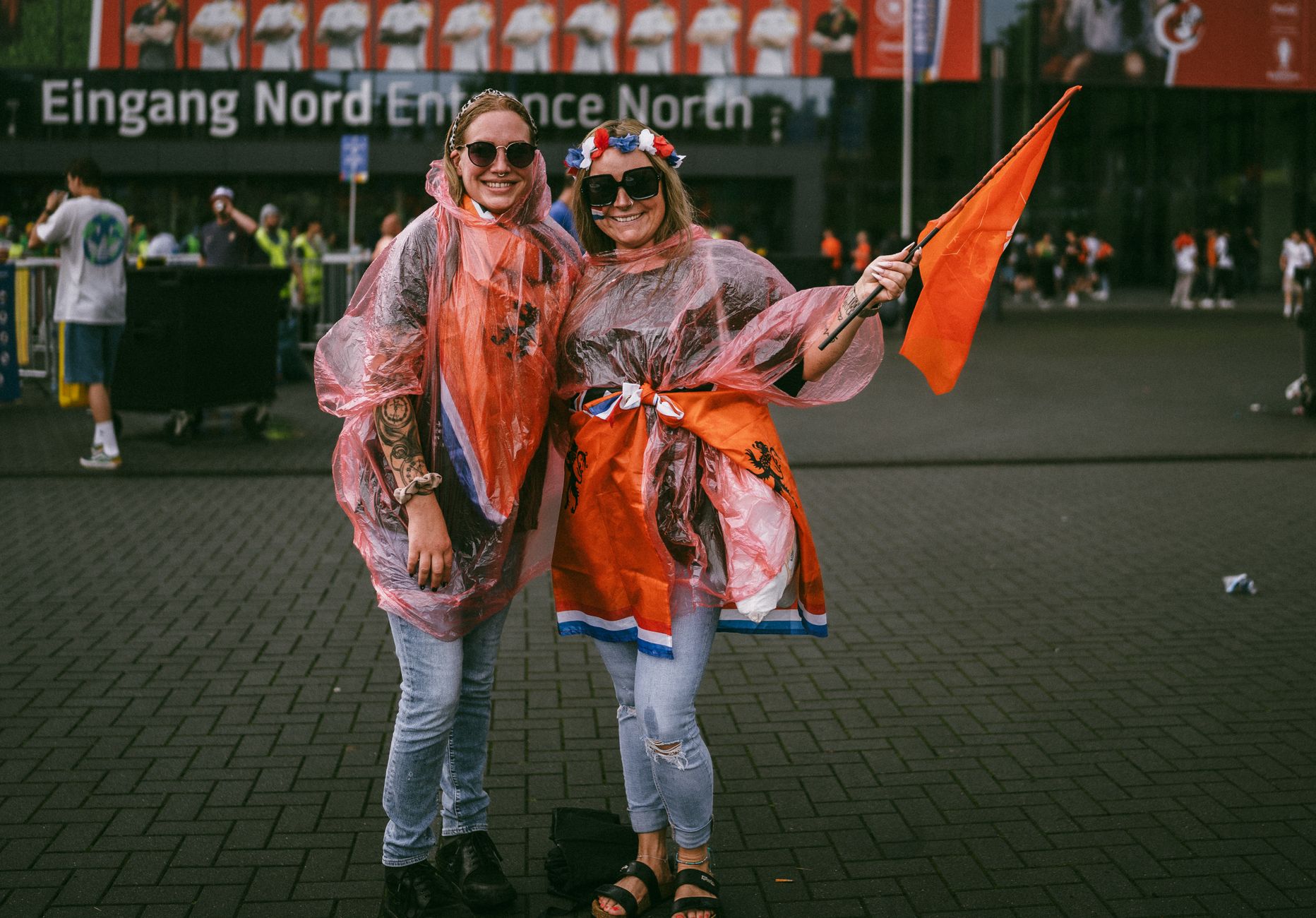 Two joyful soccer fans in raincoats and flags at a stadium entrance, enjoying a vibrant event.