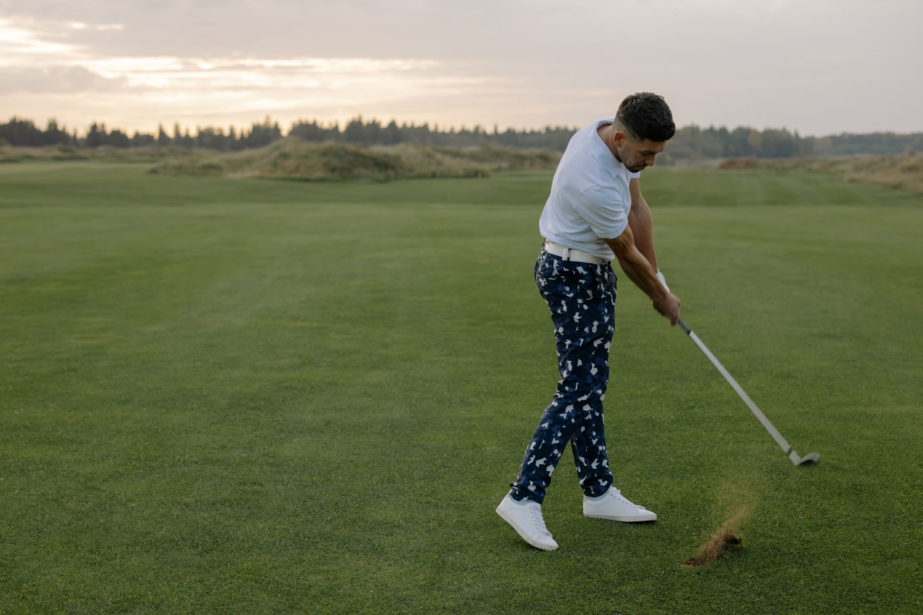 A man swings a golf club on a lush green course during sunset, capturing the essence of a serene golfing experience.