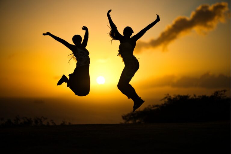 Two people jumping in silhouette against a vibrant sunset in Saint Kitts, capturing freedom and joy.