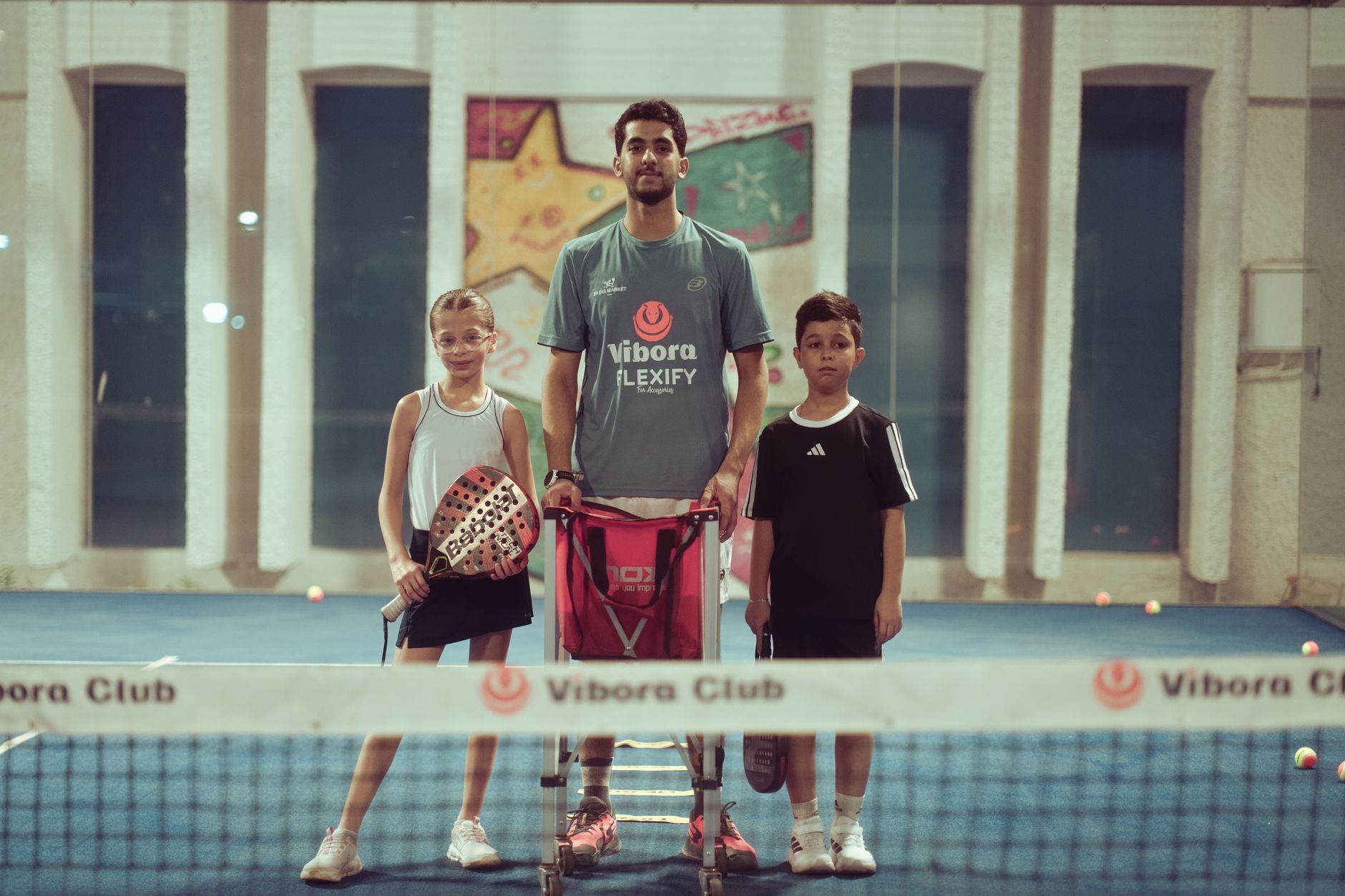 Tennis coach with two young players indoors at Vibora Club.