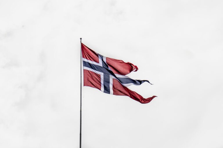 Norwegian national flag waving on a flagpole against a cloudy sky, symbolizing national pride.