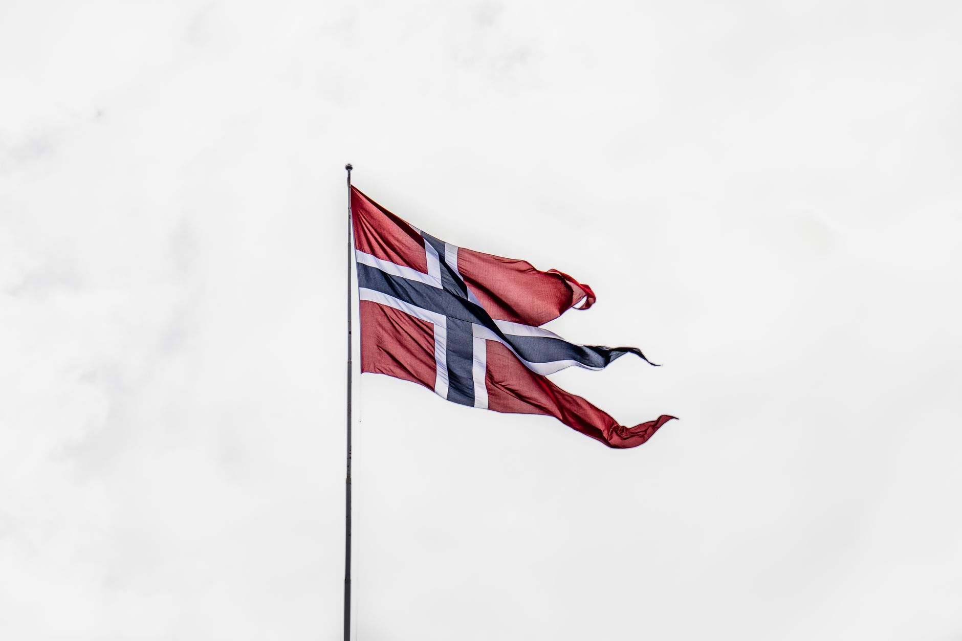 Norwegian national flag waving on a flagpole against a cloudy sky, symbolizing national pride.