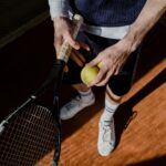A tennis player prepares for a serve, holding a racket and tennis ball on a clay court.