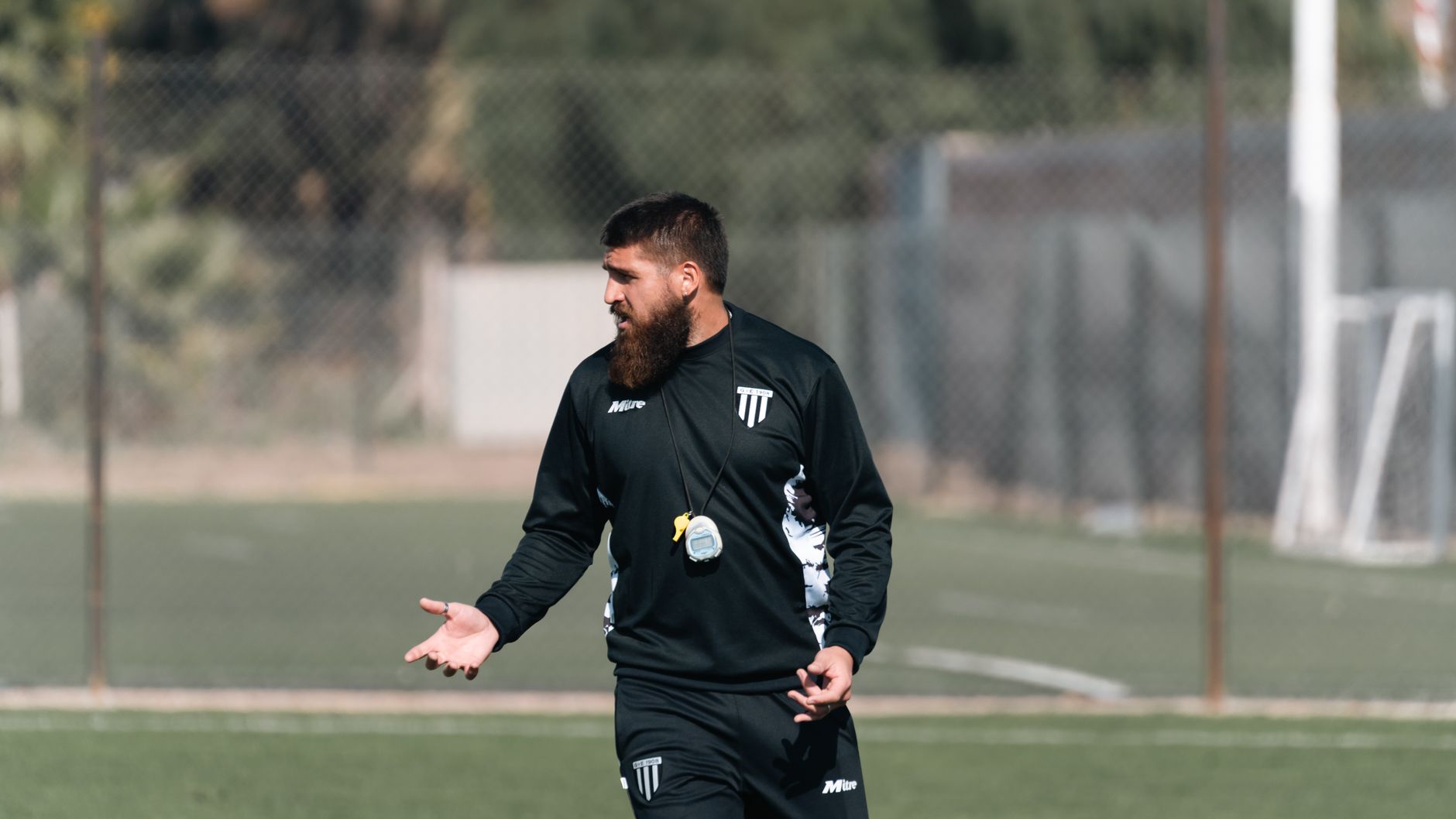 Football coach directing young players during training session on a sunny day.