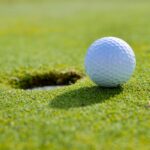 Close-up of a golf ball near the hole on a sunlit golf course green.