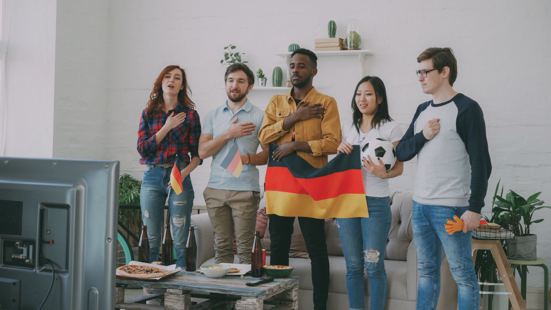 A group of friends enthusiastically supporting Germany while watching a sports event indoors.