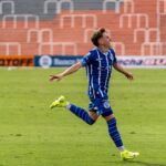 A soccer player in blue uniform celebrates after scoring a goal during a daytime match.