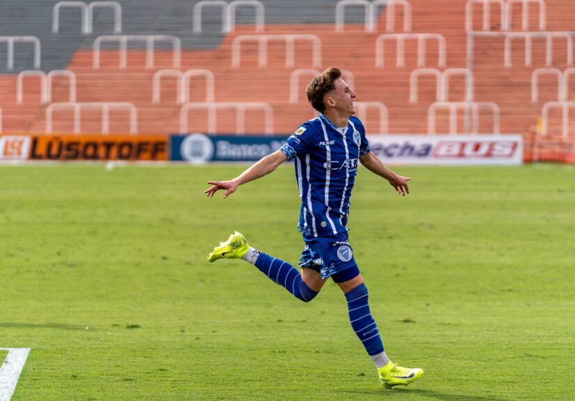 A soccer player in blue uniform celebrates after scoring a goal during a daytime match.