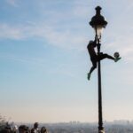 Silhouette of a man performing football tricks on a lamppost in Paris, with cityscape in the background.