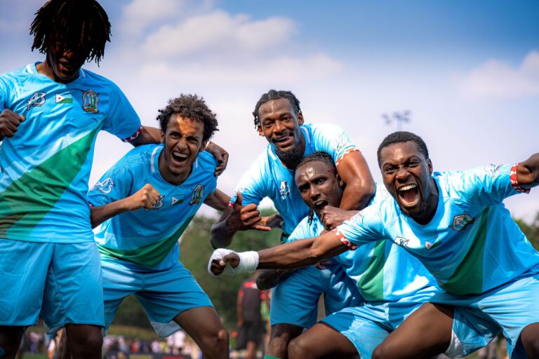 Group of soccer players joyfully celebrate victory outdoors in team uniforms.