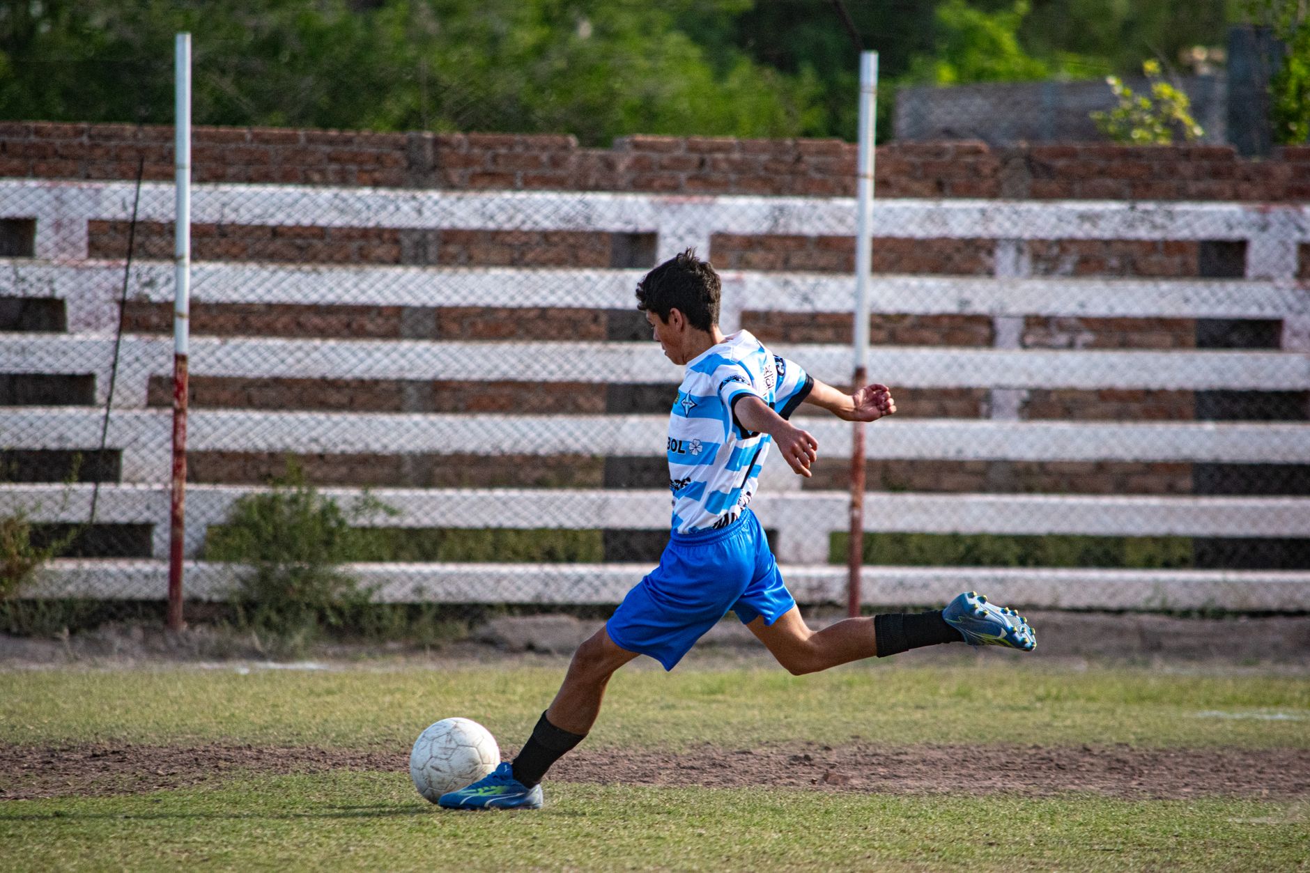 A boy kicks a soccer ball on an outdoor grassy field during the day.