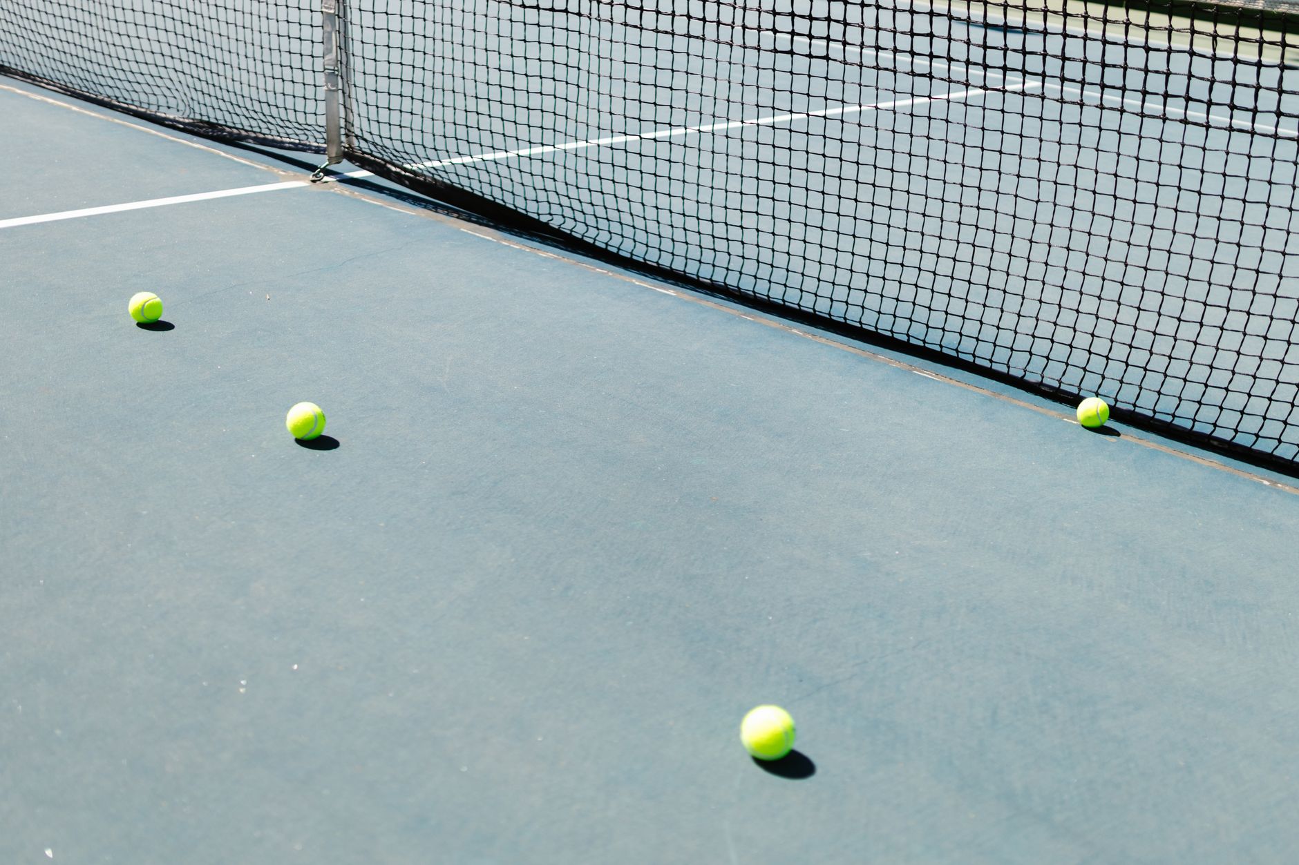 A tennis court featuring a net and several tennis balls lying on the ground, well-lit by sunlight.