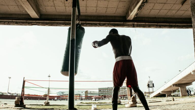 A boxer in red shorts practices punches with a hanging punching bag under a bridge in Ikeja, Nigeria.