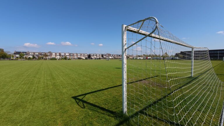 A wide view of an empty soccer field with a goal post under a clear blue sky.