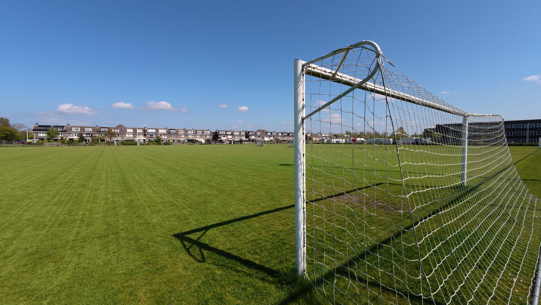 A wide view of an empty soccer field with a goal post under a clear blue sky.