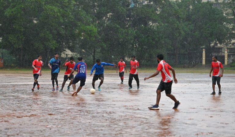 Players enjoying an intense soccer game in the rain on an open field in Kerala, India.