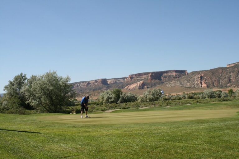 A golfer playing on a beautiful golf course set against a picturesque mountain backdrop.