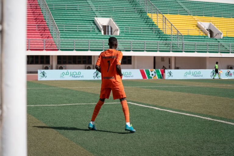 Soccer player in orange uniform on colorful stadium field during daytime game.