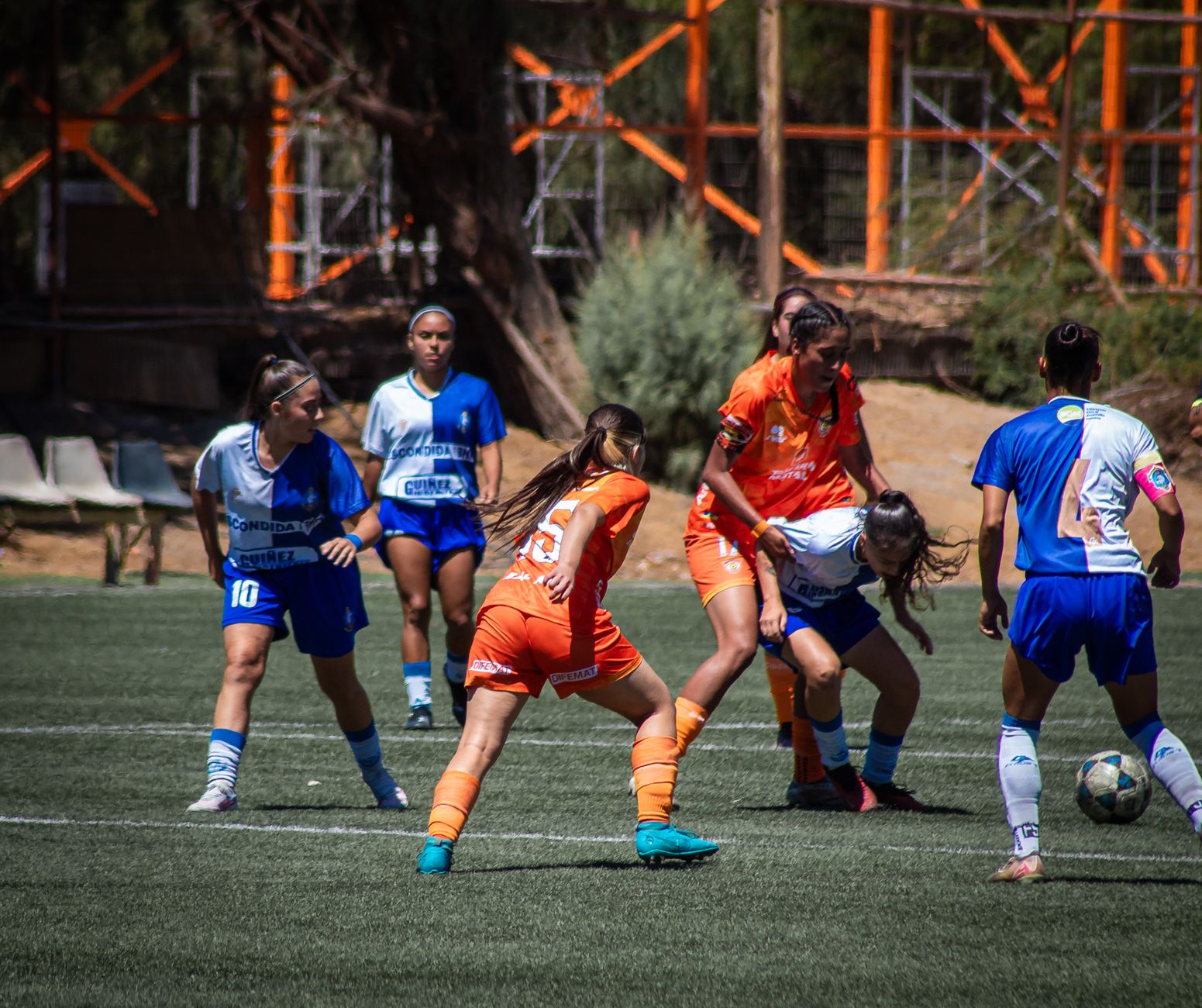 Dynamic action shot of a women's soccer game being played outdoors under bright daylight.