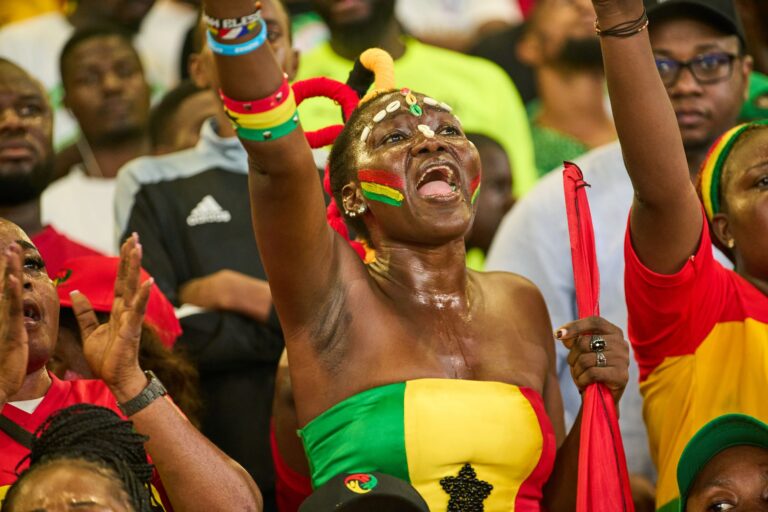 Energetic Ghanaian fan with face paint cheering passionately during a soccer match.