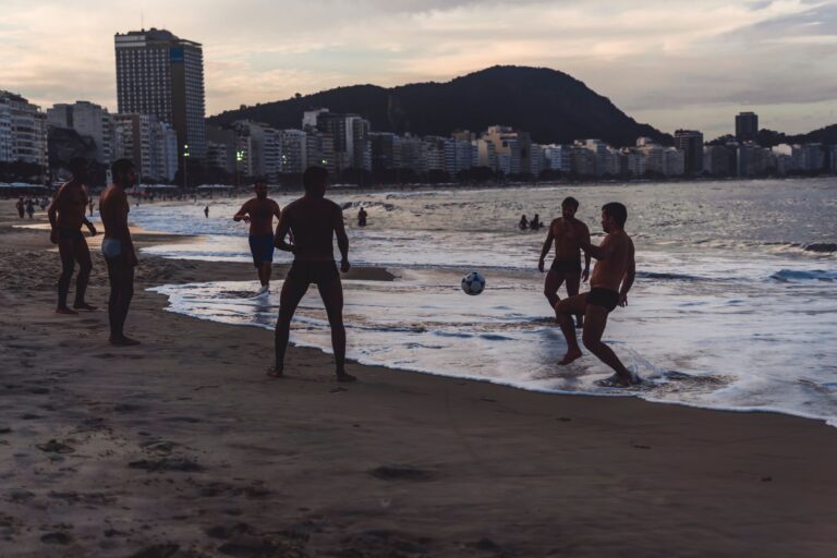 A group of friends playing soccer on Copacabana beach at sunset in Rio de Janeiro, Brazil.
