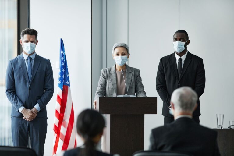 Masked business leaders at a conference podium with US flag backdrop, emphasizing safety and professionalism.
