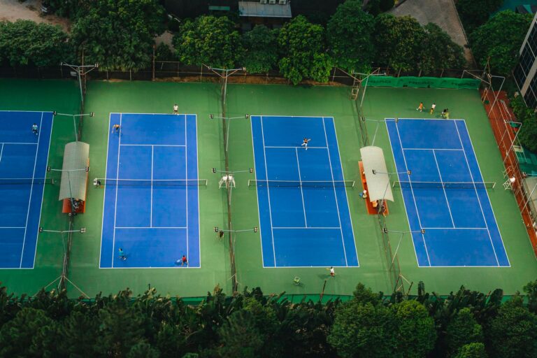 Tennis courts from above showcasing players in action, surrounded by greenery.
