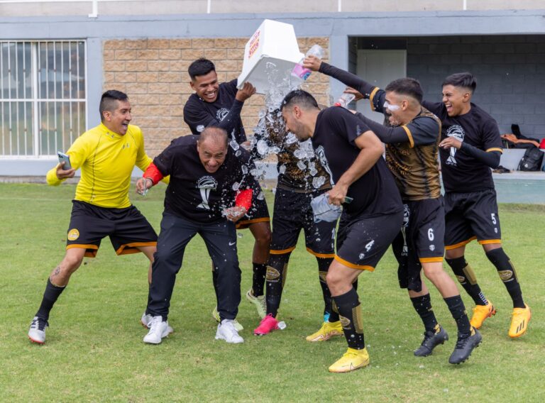 Soccer team celebrating victory with joyful water splash on field.