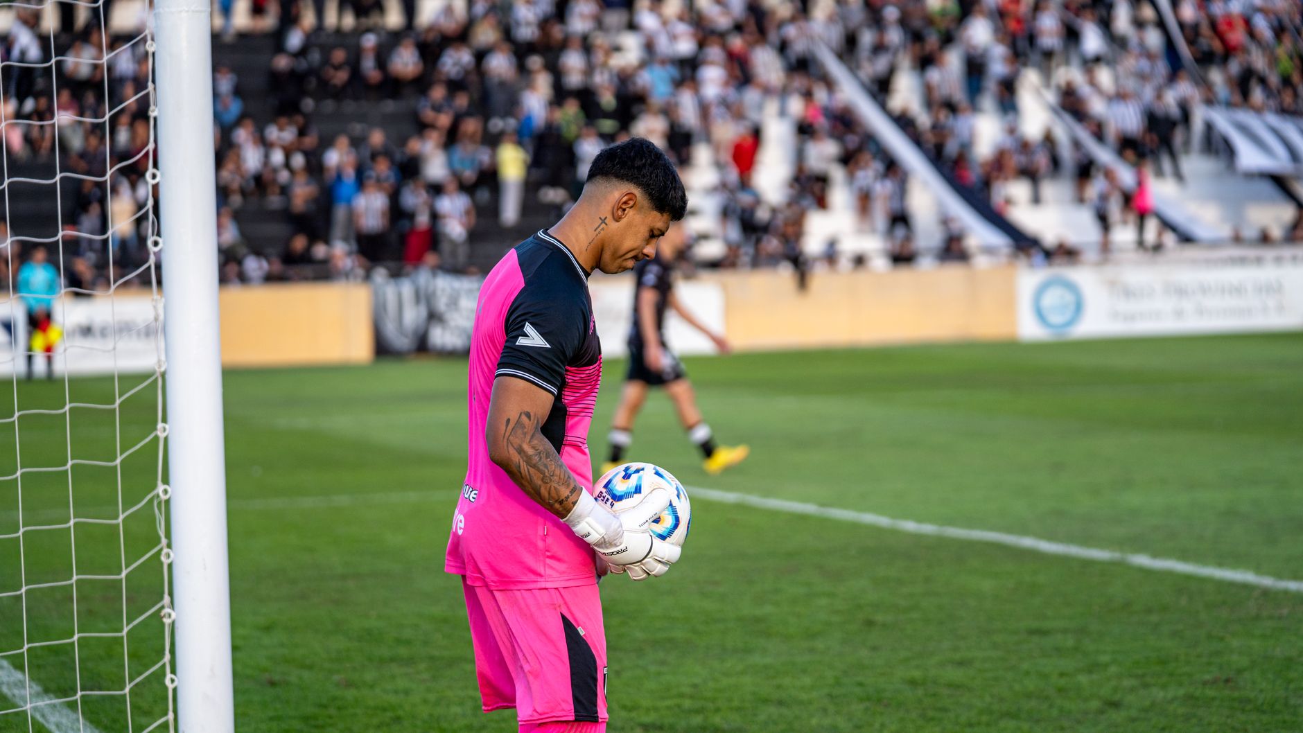 Goalkeeper in pink ready to defend during a soccer match in a packed stadium.