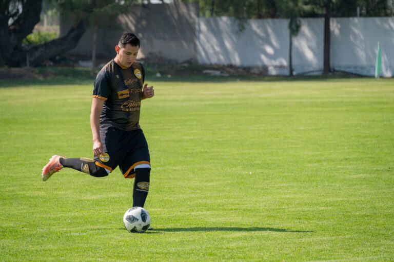 Soccer player focused on dribbling the ball during a sunny match on a green field.