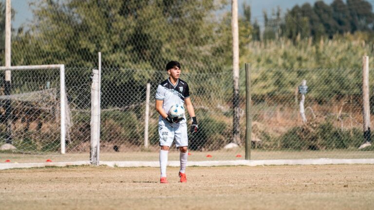 A soccer goalkeeper in uniform holding a ball during a game on an outdoor field.