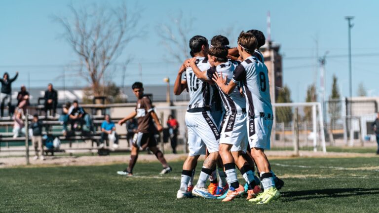 A youth soccer team in white jerseys celebrates a win on a sunny day.