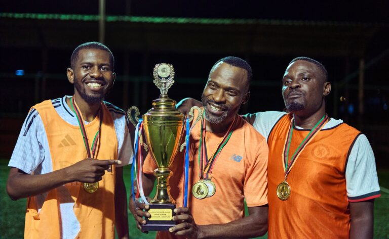 Three soccer players celebrating with medals and a trophy at night.
