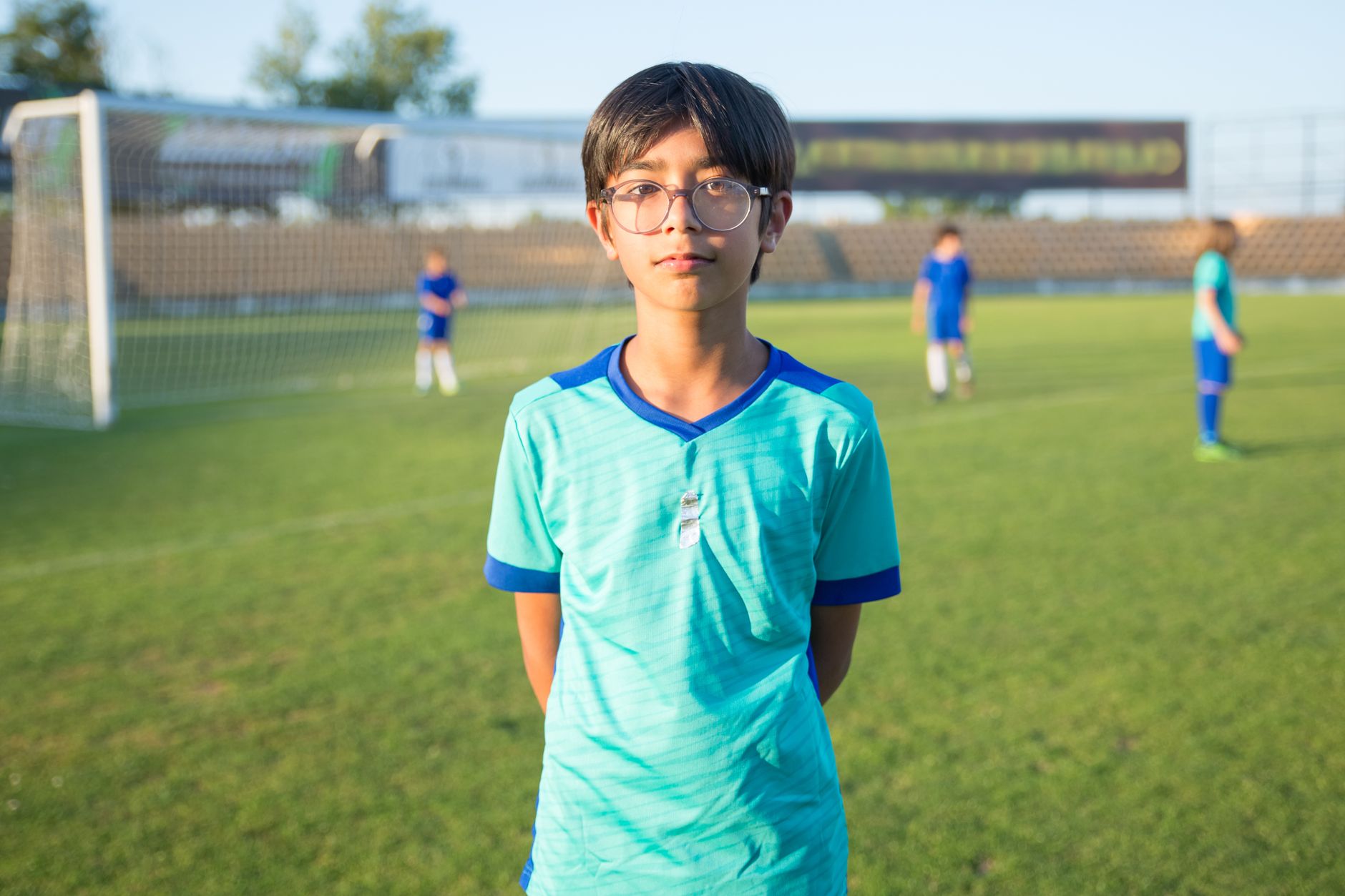 A boy standing on a sunny soccer field with teammates in Portugal.