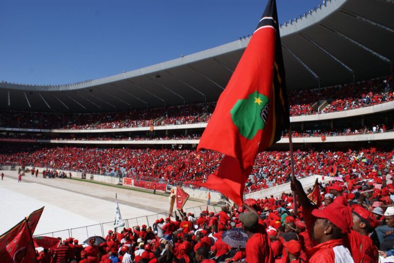 Energetic sports fans in vibrant red fill Soweto stadium during a daytime event.