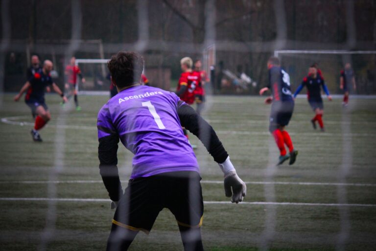Goalkeeper in purple jersey focused during an intense soccer match on a grass field.