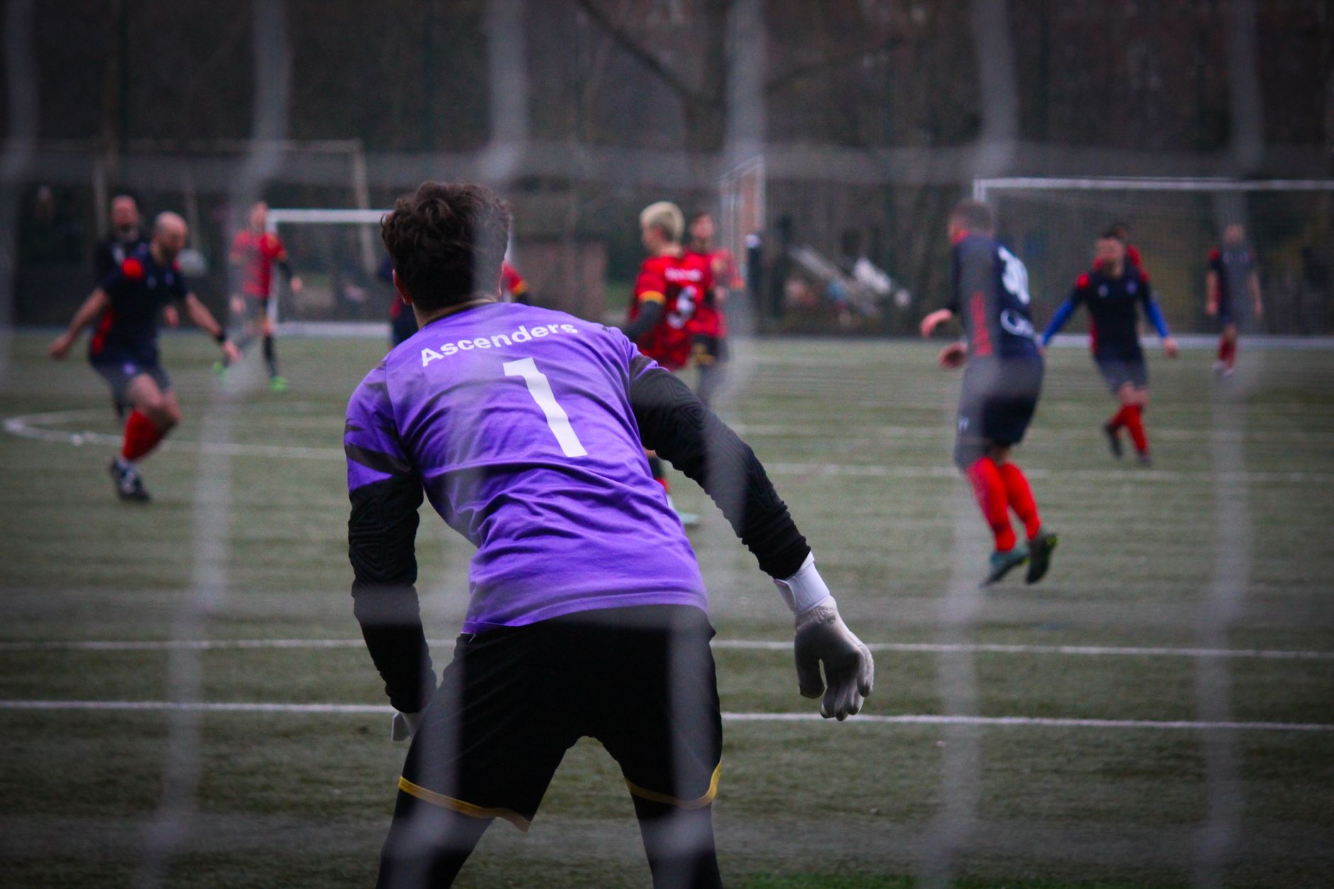 Goalkeeper in purple jersey focused during an intense soccer match on a grass field.