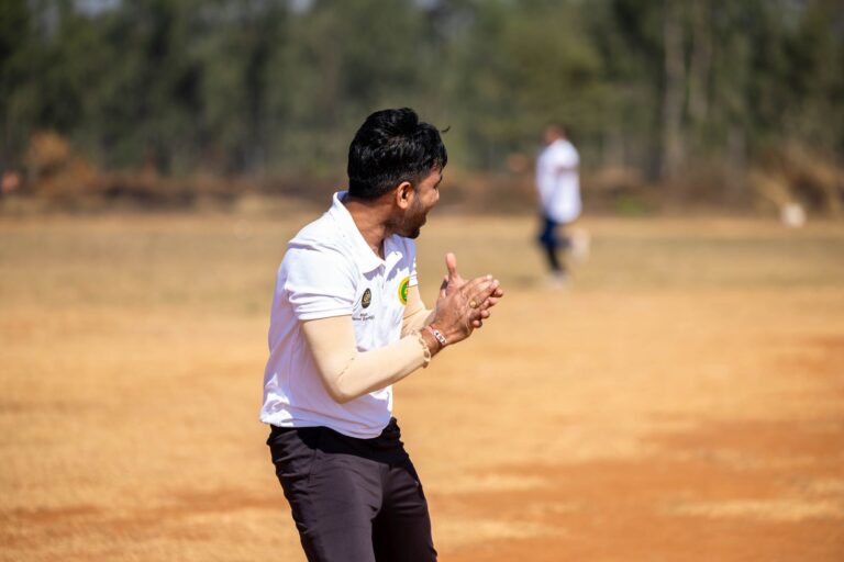 A dynamic shot of a cricketer clapping during an outdoor match on a sunny day.