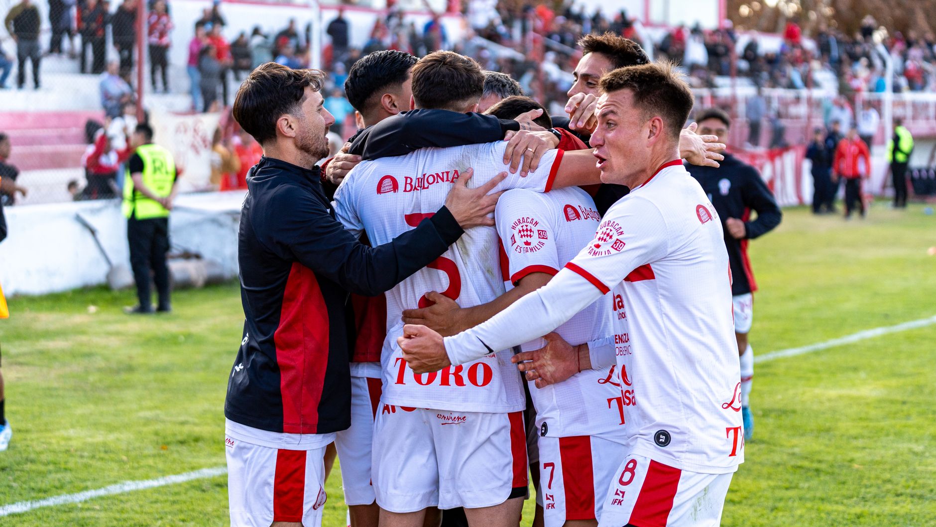 Dynamic image of a soccer team celebrating a goal during an outdoor match, highlighting teamwork and excitement.
