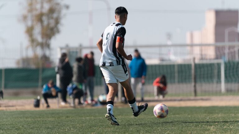 Young soccer player dribbles on field during a bright day match with spectators.