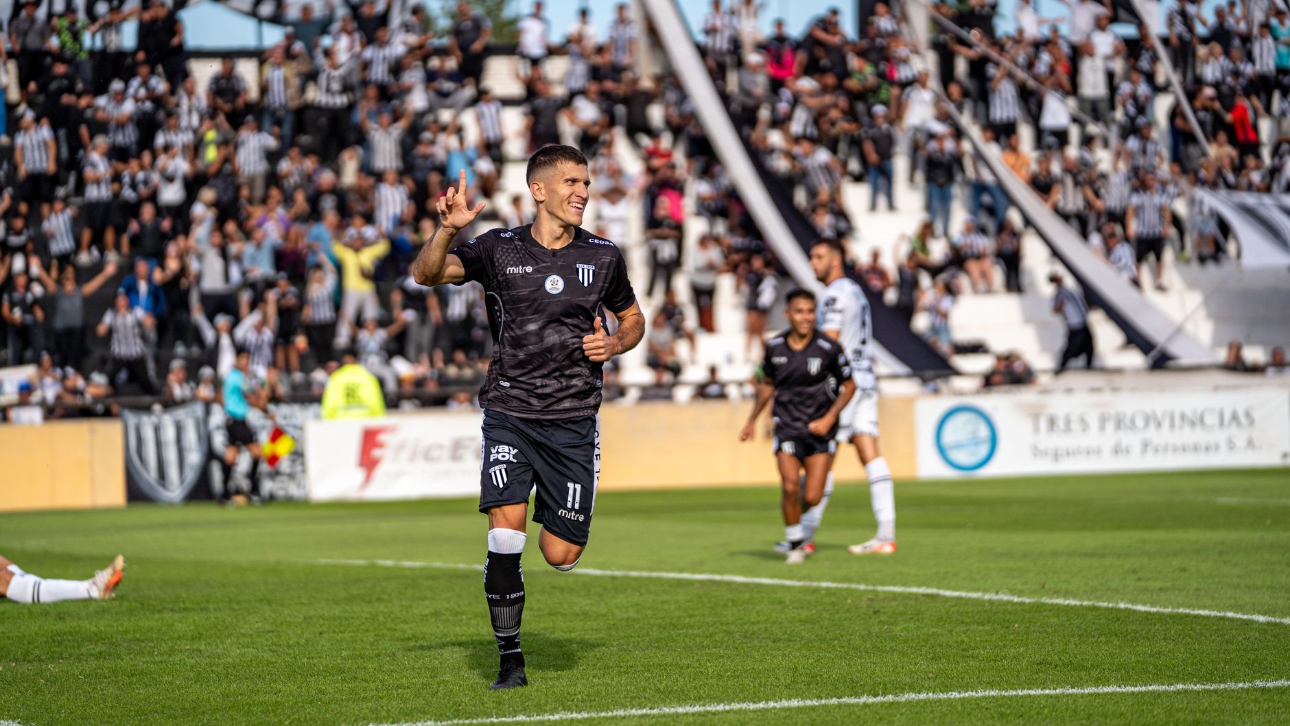 Soccer player celebrating a goal on the field with a stadium crowd in the background.